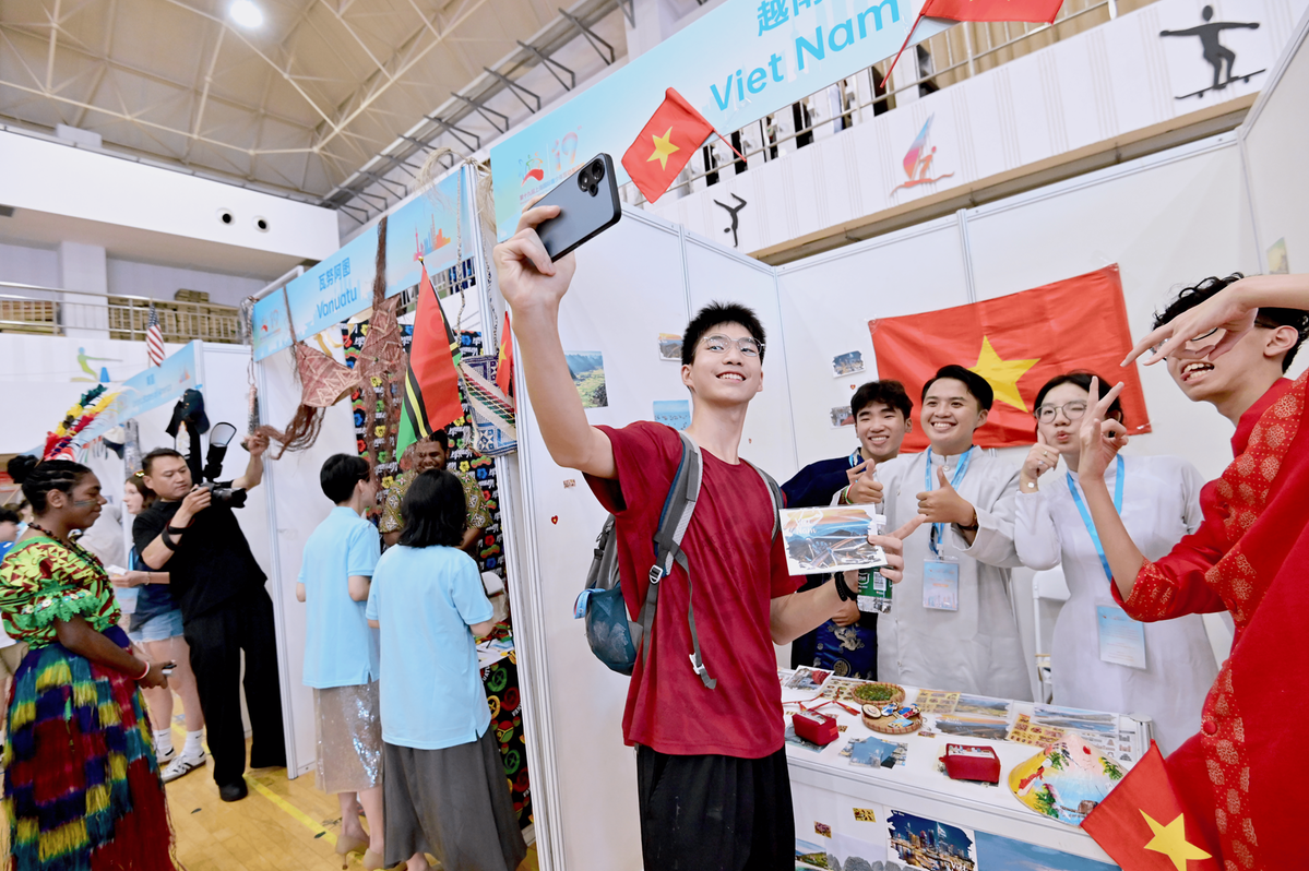 Un estudiante chino se toma un selfi grupal con campistas vietnamitas en el estand de Vietnam.png
