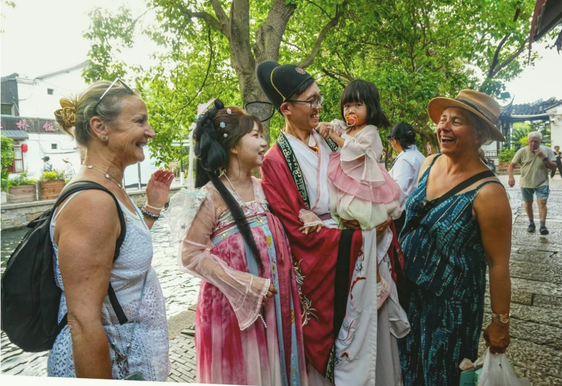 El 28 de mayo de 2026, dos turistas extranjeras interactúan con una familia china vestida con el traje tradicional hanfu en el pueblo antiguo de Zhujiajiao, en Shanghai..png