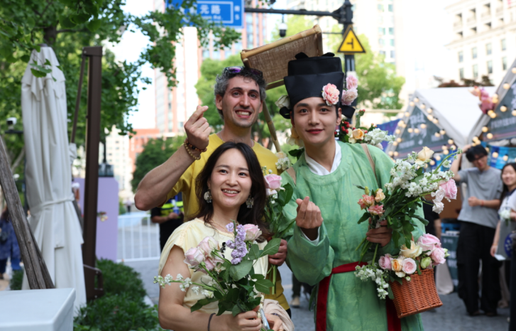 El viajero italiano Davide Cerletti y su amiga Qiu Yi posan para una foto junto a un artista que sostiene flores de Yunnan..png